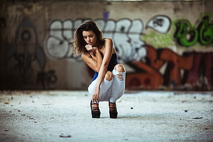 photography of a woman in blue top and white pants sitting near wall with graffiti