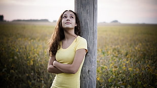 woman leaning on post near field of flowers during day