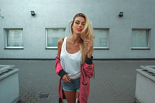 woman wearing white tank top and pink jacket standing near white building
