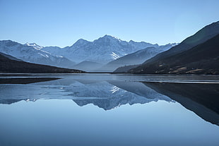 grey calm body of water near snow covered mountain at daytime