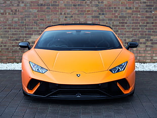 orange Lamborghini Huracan parked near brown brick wall