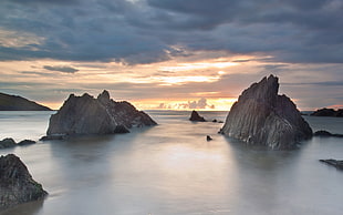 bod of water surrounded by rock formations under white cloudy sky during orange sunset