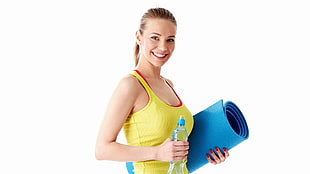 woman in yellow tank-top holding blue bottled water and rolled yoga mat