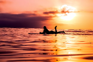 silhouette of woman lying down on paddle board during sunset HD wallpaper
