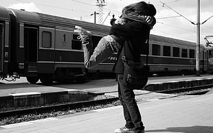 grayscale photo of couple hugging in front of train