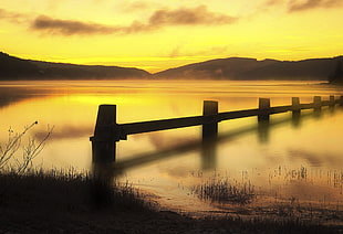 wooden dock on calm body of lake water during golden hour