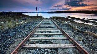 closeup photo of rusty railway near body of water during golden hour