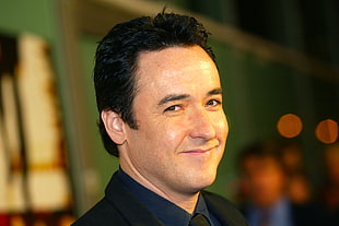 man wearing black formal suit jacket showing smirk in shallow focus photography HD wallpaper