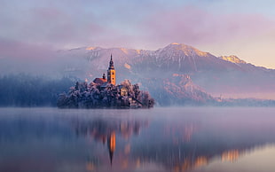 brown castle near snow covered mountain and blue calm body of water at daytime