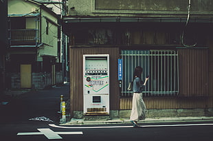 woman holding phone walking behind house and machine, Japan, cityscape, building, Asia