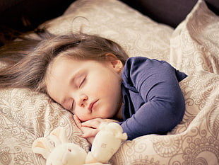toddler in black sweatshirt sleeping on beige bed
