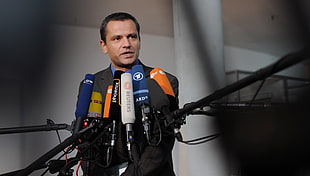 man in black suit standing beside microphones at daytime