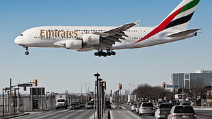 white Emirates plane below cars on road at daytime