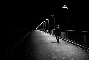 grayscale photo of man walking on pathway with light post on side
