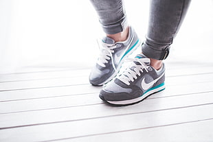 person wearing gray-white-teal Nike shoes standing on white surface