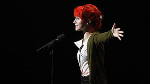 red haired woman in white button-up top standing in front of microphone while spreading her arms