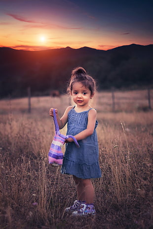 selective focus photography of girl holding bag standing on grass field