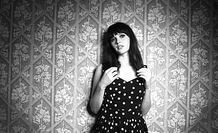 grayscale photo of woman wearing polka dot top leaning on wall