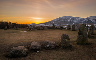 rock arrangement on grass field during golden hour and mountain at distance