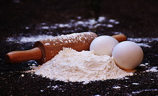 brown wooden rolling pin beside two white eggs and flour