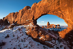 photo of brown arch mountain near ocean during day time