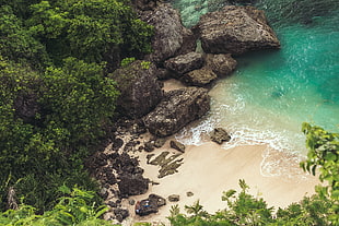 aerial photo of white sand beach beside big black stones and green water