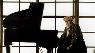 man with brown newsboy cap sitting next to grand piano
