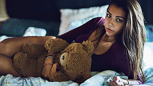 woman lying on bed holding brown bear plush toy