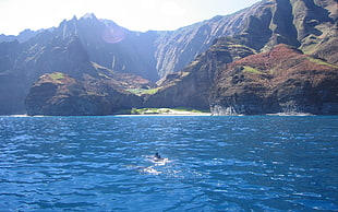 person swims on sea near mountain during daytime
