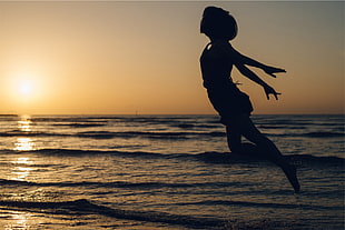 silhouette of woman jumping near ocean water during yellow sunset
