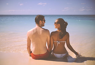couple sitting beside each other on sand beside ocean during daytime