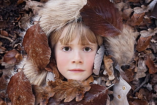 closeup photography of girl's face surrounded by dried leaves