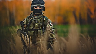 tilt-shift photography of person in green military outfit holding black rifle during daytime