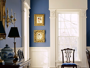 two gold-colored framed paintings near window with white frame