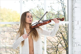 woman wearing white cardigan playing violin during daytime