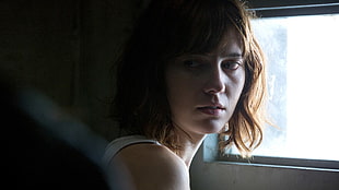 woman wearing white sleeveless shirt beside 1-pane window