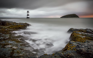 photography of black mountain and lighthouse near body of water, penmon