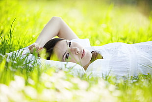 shallow focus photography of woman in white dress lying on green grass field