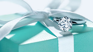 silver-colored diamond solitaire ring on top on gift box
