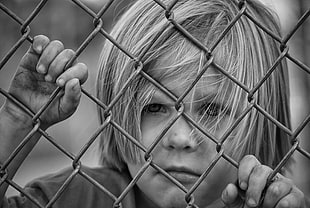 gray scale photo of boy holding chain-link fence