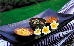 rectangular black wooden platter with three white-and-yellow petaled flowers and three round brown wooden bowls