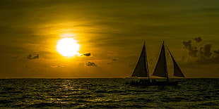 silhouette photo of a two sailboats in bodies of water with sun background