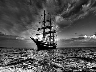 grayscale photo of a sailing ship on body of water under moving clouds
