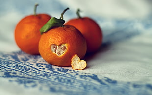three orange fruits on white textile