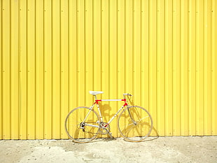 white and red rigid bike parked beside yellow painted wall
