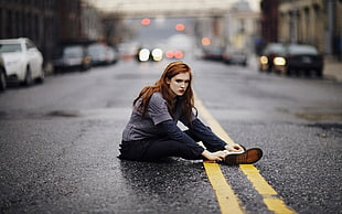 woman in gray sweater and black pants lying on asphalt road