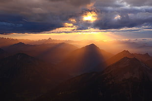 mountains under cloudy skies with sun rays