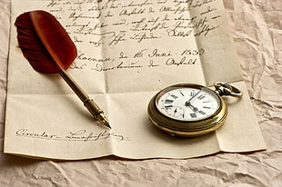 brass-colored pocket watch near ink pen