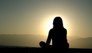 woman's silhouette sitting on top of mountain under clear sky during daytime