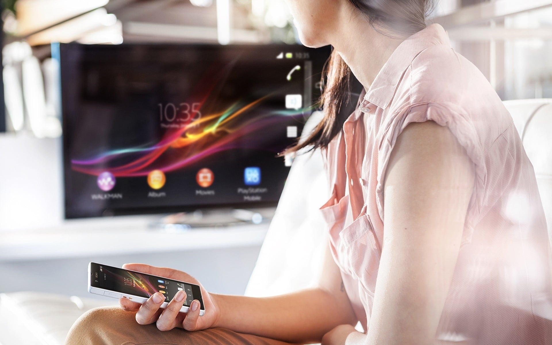 woman in pink sleeveless button-up top holding white smartphone looking at black LED TV